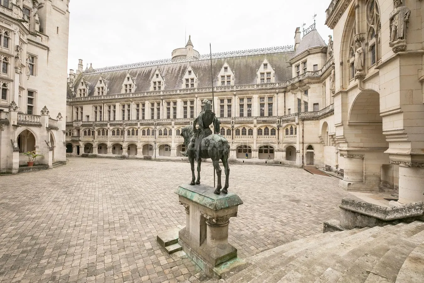 La statue d'un cheval et de son cavalier se trouve au centre d'une grande cour en pierre, entourée par l'hôtel historique de Harlay à Compiègne, avec ses fenêtres cintrées et ses sculptures détaillées.