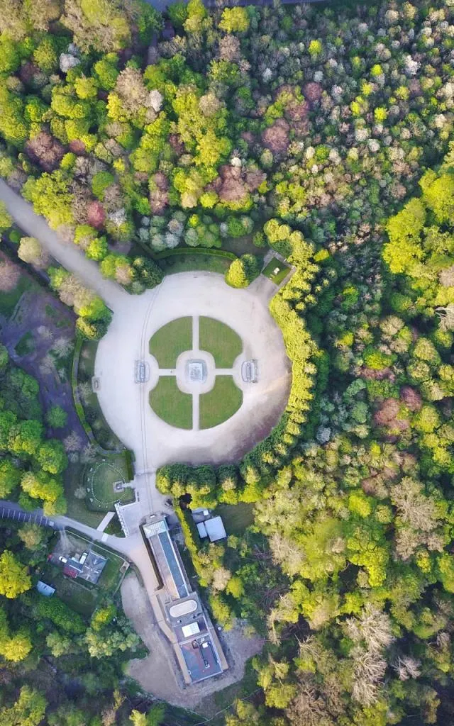 Vue aérienne d'une place circulaire avec des allées, entourée d'une forêt verte dense et de bâtiments proches, dont le célèbre Hôtel de Harlay, une option bien connue d'Hébergement Compiègne, au bas de l'image.