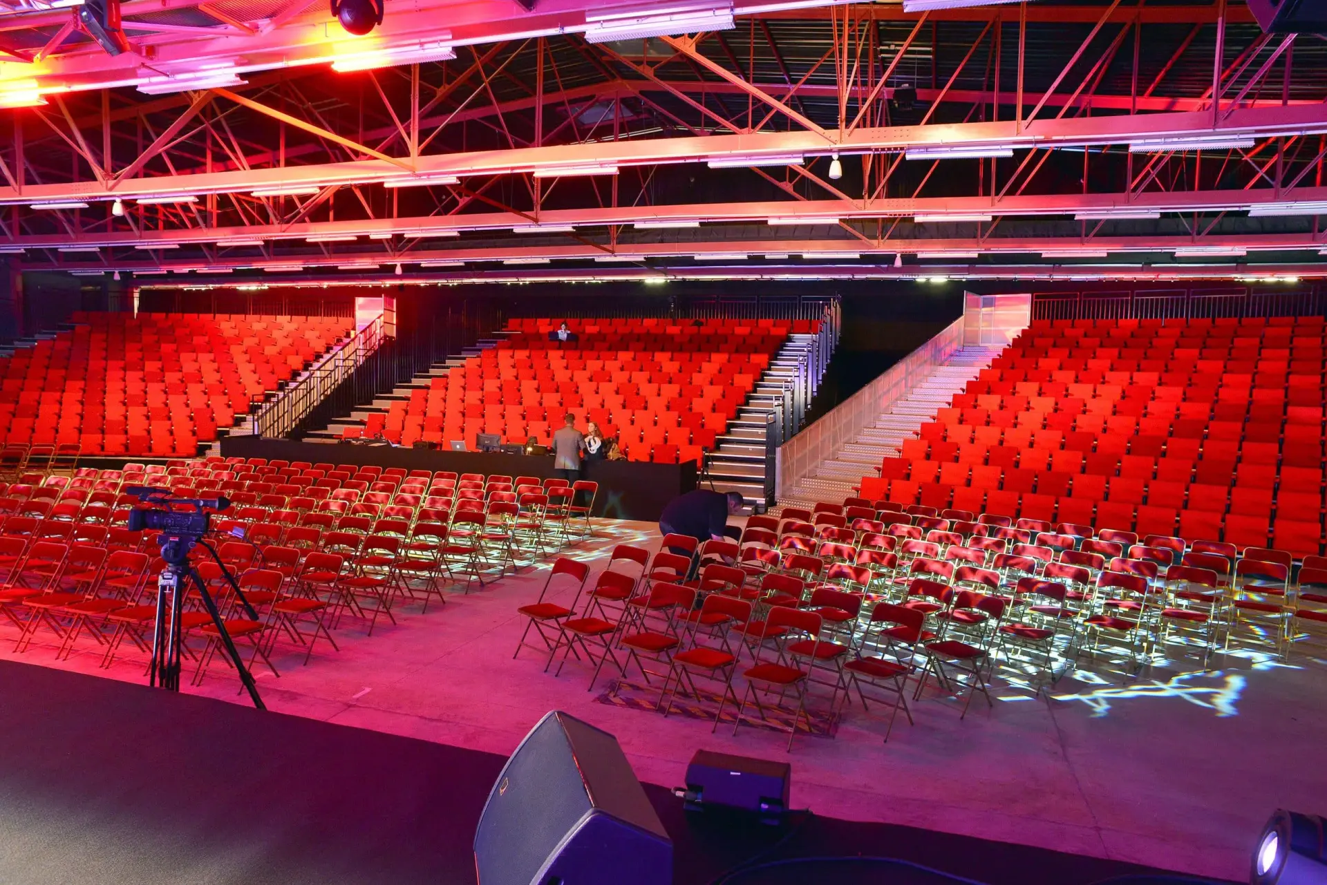 Auditorium intérieur vide avec des rangées de sièges rouges, des chaises pliantes devant, et une scène au premier plan - un lieu d'événement idéal près de l'Hôtel à Compiègne, avec un éclairage zénithal qui illumine l'espace spacieux.