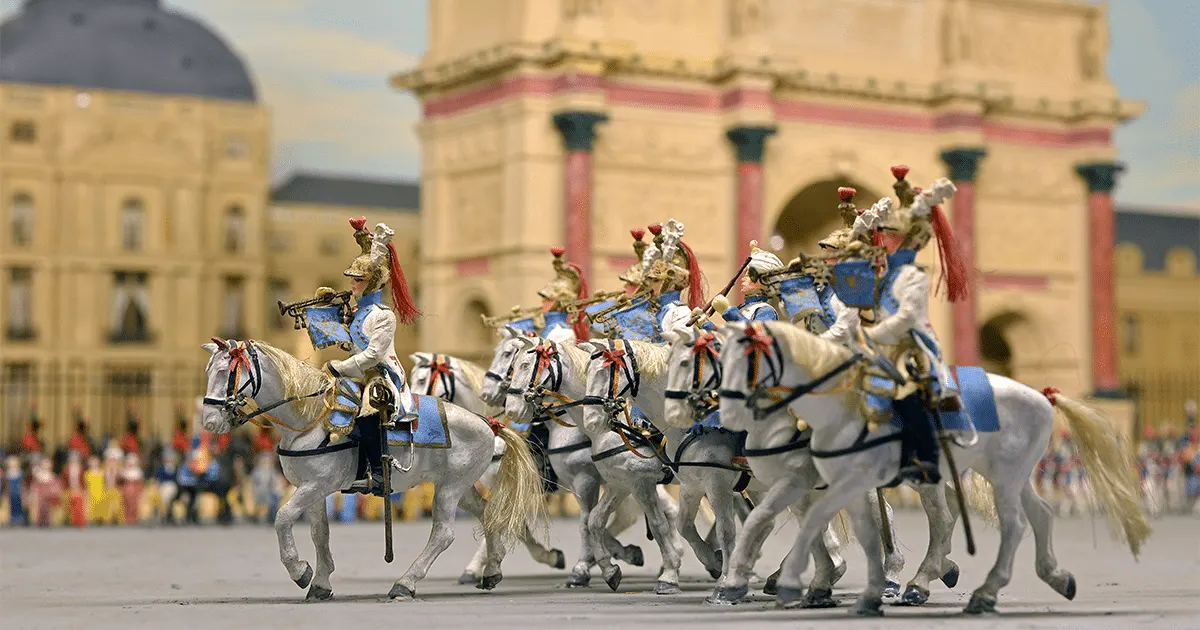 Un groupe de petits soldats en uniformes ornés montent des chevaux blancs en formation, avec en arrière-plan une maquette détaillée de l'Hôtel de Harlay, un bâtiment classique.
