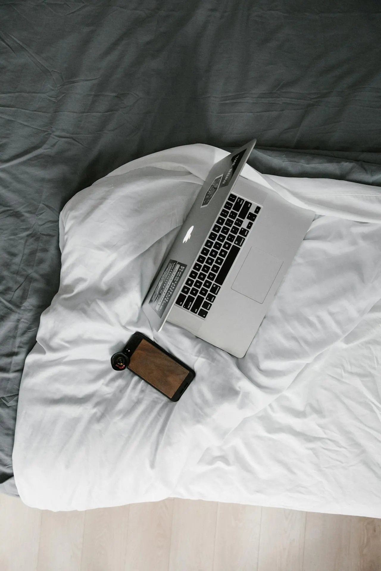 Ordinateur portable et téléphone posés sur un lit aux draps blancs