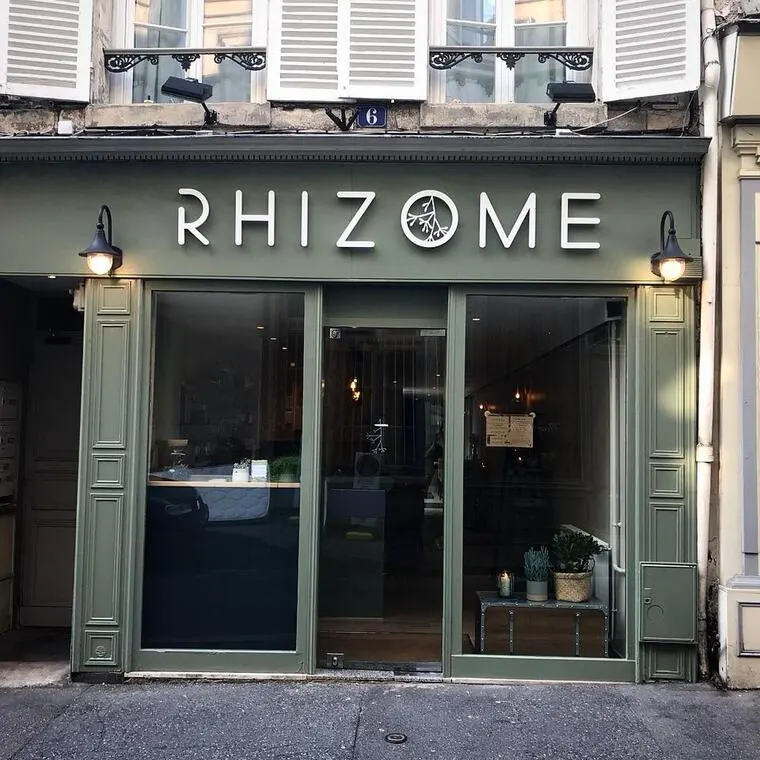 L'extérieur de RHIZOME, près de l'Hôtel de Harlay, se caractérise par de grandes portes vitrées, des plantes en pot à l'entrée et deux appliques murales de part et d'autre de l'enseigne. Idéal pour les visiteurs à la recherche d'endroits uniques lors de leur découverte de l'Hébergement Compiègne.