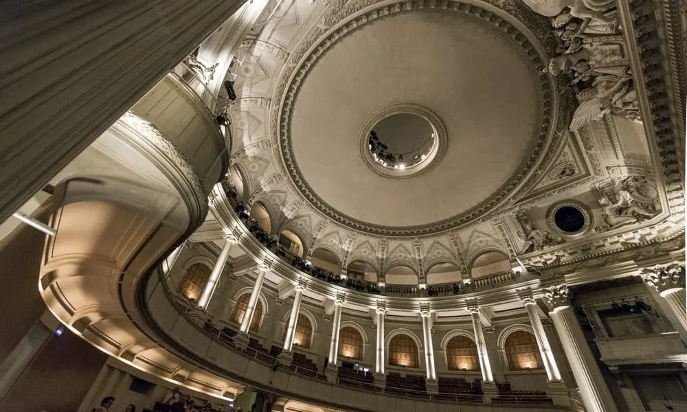 Vue d'un plafond en dôme orné et des balcons supérieurs à l'intérieur d'un grand théâtre classique ou d'une salle de concert dans le style de l'Hôtel de Harlay, éclairé par une lumière douce.